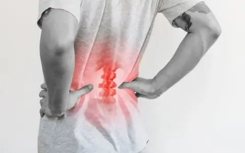 Osoba odczuwa m54 bóle grzbietu, trzymając się za bolące lędźwie. Czerwony obszar podkreśla problem.