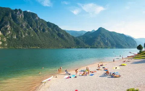 Spiaggia affollata sui laghi in Piemonte, ideale per una gita in moto. Montagne verdi e acqua azzurra.