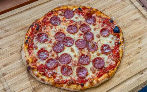 Eine köstliche Pizza Salami mit geschmolzenem Käse und knusprigem Rand liegt auf einem Holzbrett.