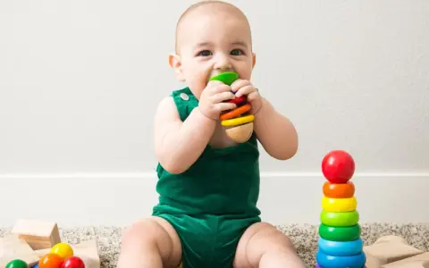 Uśmiechnięte dziecko w zielonym ubranku odkrywa świat, kiedy dziecko chwyta zabawki. Kolorowe klocki i pierścienie zachęcają do zabawy.