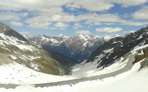 Strada tortuosa sulla Ötztaler Gletscherstraße, tra montagne innevate e cielo azzurro con nuvole bianche.