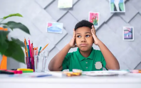 Niño frustrado con las manos en la cabeza, rodeado de materiales de arte, quizás lidiando con problemas de aprendizaje.
