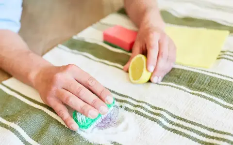 Ręce czyszczą dywan z plam po jagodach, używając sody i cytryny.