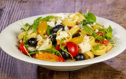 Un piatto di pasta alla crudaiola con pomodorini, olive nere, rucola e scaglie di parmigiano. Fresca e colorata.