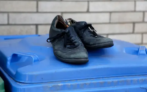 Stare czarne buty na niebieskim koszu na śmieci. Zastanawiasz się, gdzie wyrzucić buty gumowe? To nie są gumowe, ale też już zużyte.