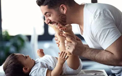 Ein lachender Vater mit Kind spielt liebevoll mit den Füßen seines Babys.