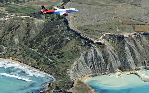 Samolot linii Malta Air przelatuje nad malowniczym wybrzeżem. Widok z lotu ptaka na maltańskie lotniska i krajobraz.