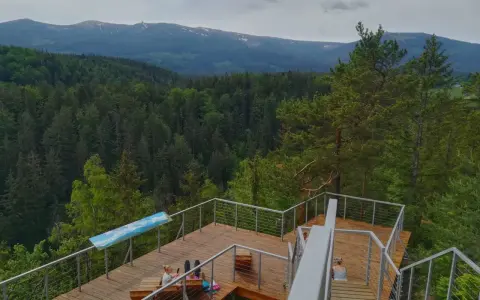Drewniany punkt widokowy w Karpaczu z widokiem na góry i las. Dwie osoby odpoczywają na tarasie.