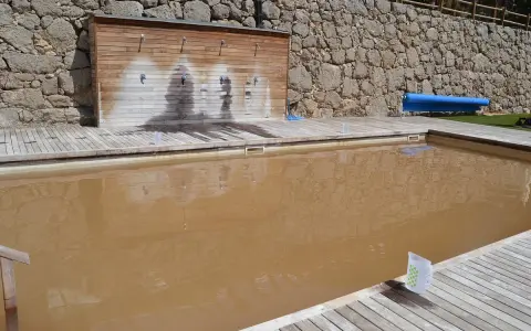 Piscina de sal con agua turbia y rodeada de madera. Al fondo, una pared de piedra y duchas.