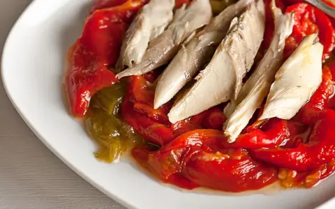 Pimientos asados rojos y verdes con trozos de pescado blanco encima, servidos en un plato blanco.