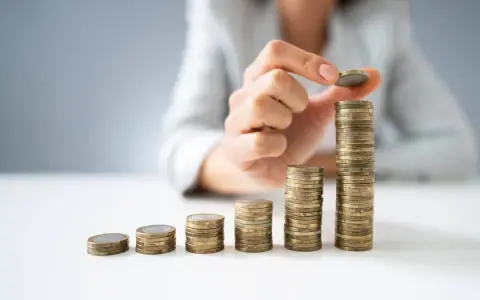 Dłoń układa monety w rosnące słupki, symbolizując wzrost wartości. To wizualizacja zarządzania finansami i optymalizacji faktoring kosztów.