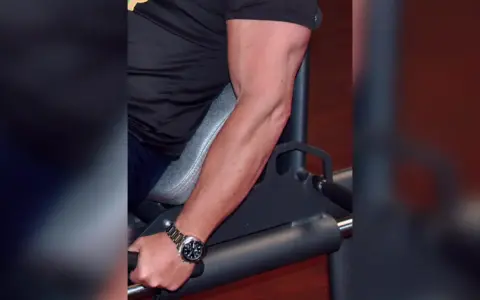 Mann trainiert unterarme im gym. Sein Bizeps ist gut sichtbar, während er sich auf ein Gerät stützt.