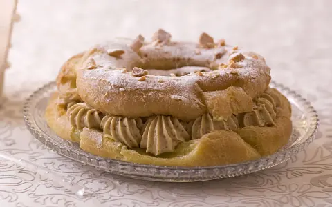 Un Paris-Brest généreusement garni de crème pâtissière au caramel beurre salé, saupoudré de sucre glace et d'amandes effilées.