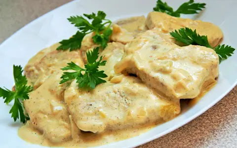 Filet z indyka w sosie śmietanowym, udekorowany natką pietruszki, prezentuje się apetycznie na białym talerzu.