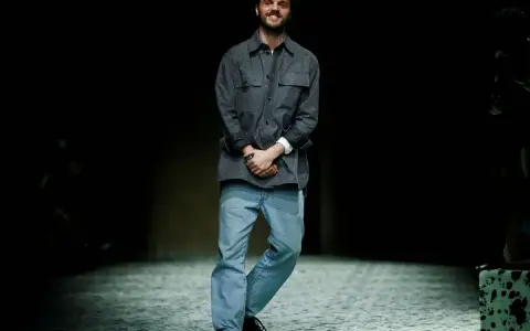Matthieu Blazy, diseñador de Bottega Veneta, sonríe en la pasarela con camisa gris y vaqueros.