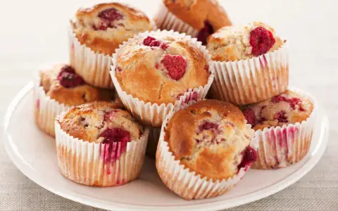 Stos muffinek z malinami na białym talerzu.