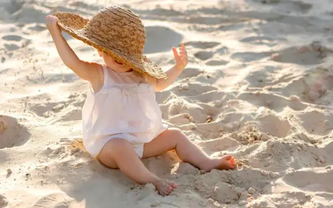 Liten bebis med stråhatt på stranden, njuter av solens värme.