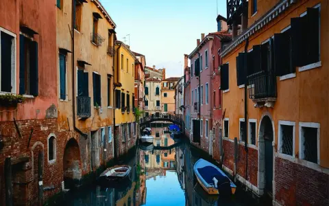 Bunte Häuser säumen einen Kanal in Venedig. Kleine Boote treiben auf dem Wasser. Ein kleiner Bogenbrücke überspannt den Kanal. Das ist, was man in Venedig gesehen haben muss.