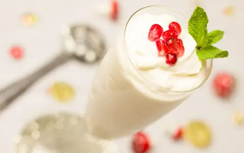Creme double in einem Glas, garniert mit Granatapfelkernen und Minze. Ein Löffel liegt daneben.