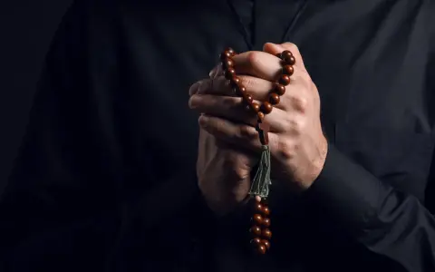 Dłonie księdza trzymające paciorki różańca, symbol wiary i nadziei w obliczu trudów życia, gdzie pańszczyzna a kościół splatały się w historii.