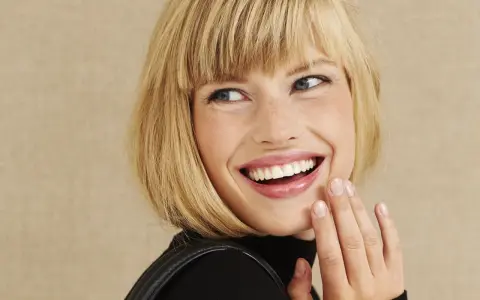 Frau mit blondem Bob, die lacht und ihre Hand vor den Mund hält. Perfekt gestylter Bob.