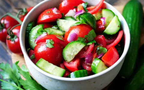 Frischer Tomaten-Gurken-Salat mit roten Zwiebeln und Petersilie, garniert mit ganzen Kirschtomaten und Gurken.