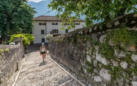 Una donna sale una scalinata di ciottoli verso un edificio bianco, un percorso che ricorda la salita alla Madonna della Corona.