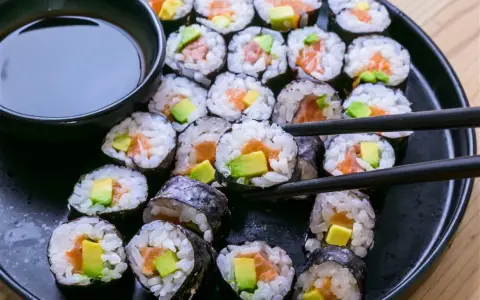 En tallrik med hemgjord sushi, perfekt för ett enkelt sushi recept. Lax och avokado rullade i ris och nori, med en skål sojasås.
