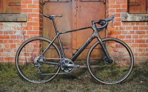 A sleek black Salsa Warroad gravel bike with orange accents stands against a rustic brick wall and weathered metal door.