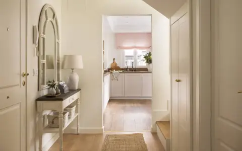 Un recibidor luminoso con espejo arqueado, consola con cestas y una cocina al fondo. ¡Ideal para pintar recibidor y darle un toque fresco!
