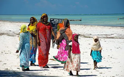 Kobiety w kolorowych strojach spacerują po plaży. Czy Zanzibar to kraj? Tak, to wyspa w Tanzanii.