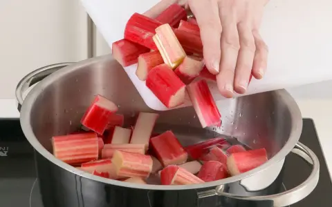 Rhabarberstücke werden von einem Schneidebrett in einen Topf mit Wasser geschüttet. So beginnt das Rhabarber verarbeiten für Kompott oder Kuchen.
