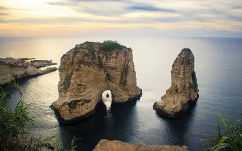 Felsformationen im Meer vor der Küste von Beirut Stadt, mit einem kleinen Boot, das durch den Felsbogen fährt.