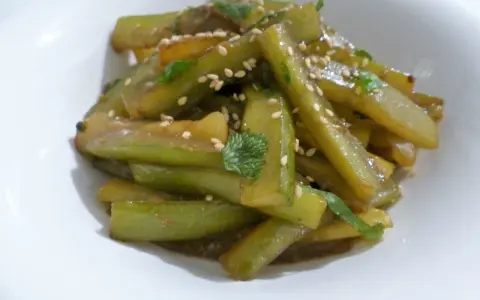 Délicieuse recette concombre cuit, garnie de graines de sésame et de persil frais, servie dans un bol blanc.