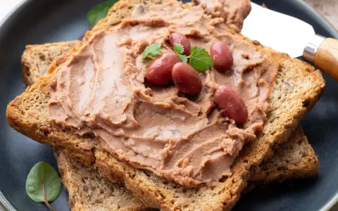 Pyszna pasta z czerwonej fasoli na chrupiących tostach, ozdobiona fasolkami i listkami ziół. Idealna na szybkie śniadanie.