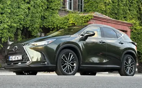 Ciemnozielony Lexus NX 450h+ plug-in zaparkowany przed budynkiem porośniętym bluszczem.