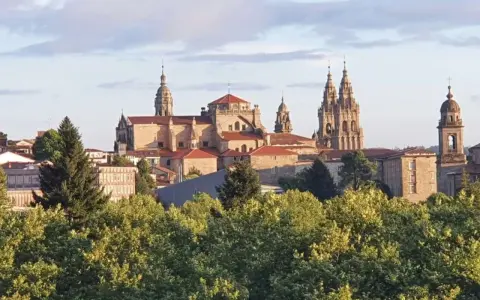 Majestatyczna katedra w Santiago de Compostela, cel pielgrzymek, wyłania się zza zieleni drzew.