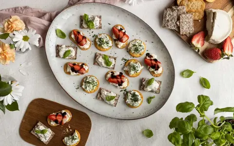 Vackra midsommar-snittar med ost, jordgubbar och örter på en stor tallrik. Perfekt för sommarfesten!