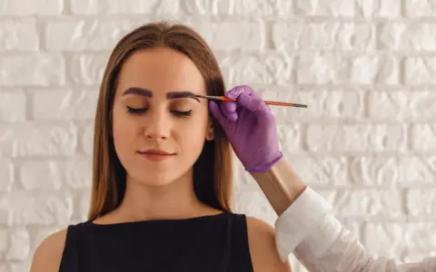 Korekta zbyt ciemnej henny na brwiach. Stylistka nakłada produkt rozjaśniający.