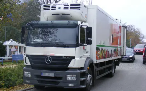 Biały Mercedes Axor z chłodnią, ozdobiony grafiką warzyw, gotowy do dostawy świeżych produktów.