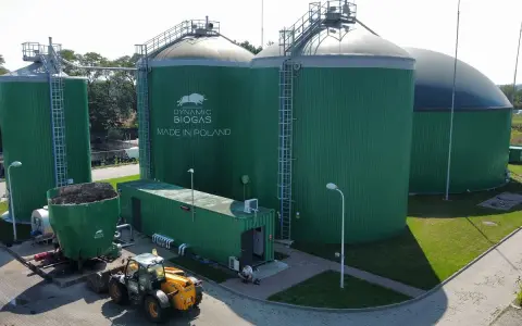 Zielone zbiorniki instalacji biogazowej, z logo "DYNAMIC BIOGAS MADE IN POLAND". Obok ładowarka i kontener.