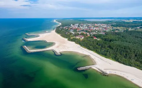 Malownicze plaże w Polsce z kamiennymi falochronami, zielonymi wodami Bałtyku i nadmorskim miasteczkiem w tle.