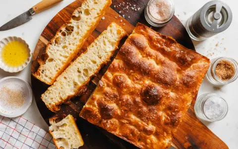 Goldbraune Focaccia mit grobem Salz, bereit zum Belegen. Daneben Olivenöl, Gewürze und ein Messer.