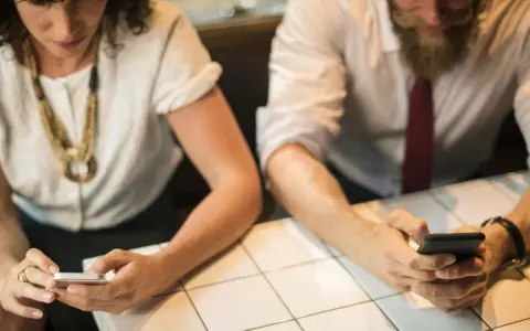 Zwei Personen sitzen an einem Tisch und schauen auf ihre Smartphones.