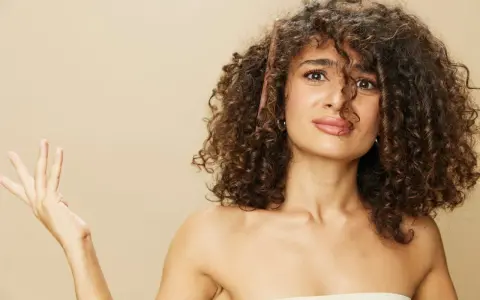 Une femme aux cheveux bouclés tente de diminuer le volume de sa chevelure avec un peigne.
