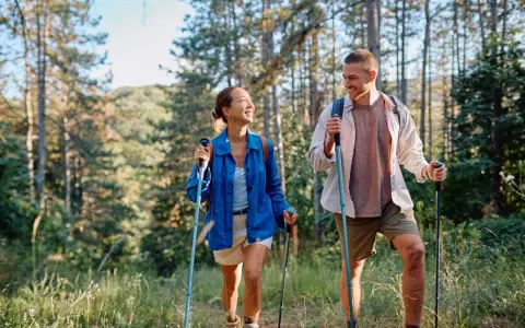 Coppia sorridente fa nordic walking tra gli alberi, godendosi i benefici di questa attività all'aria aperta.