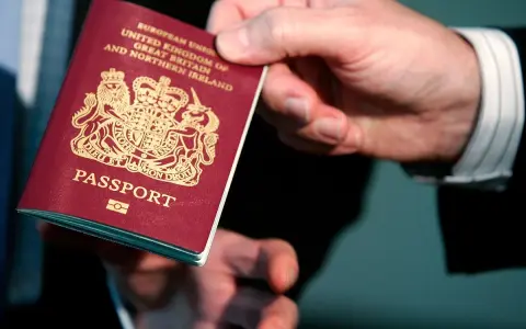 Dłoń podaje paszport biometryczny Wielkiej Brytanii. Widoczny herb i napis "PASSPORT".