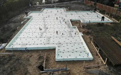 Budowa domu: przygotowane słupy fundamentowe, zbrojenie i izolacja płyty fundamentowej.