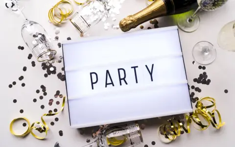 Świętowanie zaczyna się od zaproszeń! Na stole leżą kieliszki, szampan i konfetti, a tablica świetlna głosi "PARTY".