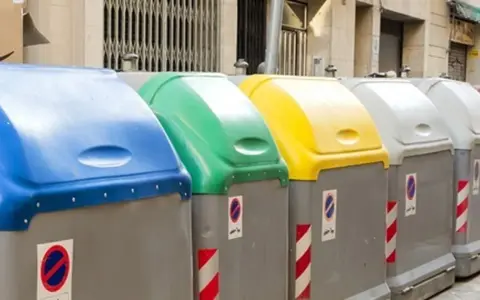 Fila de contenedores de reciclaje de Ecoembes en la calle: azul, verde, amarillo y grises.